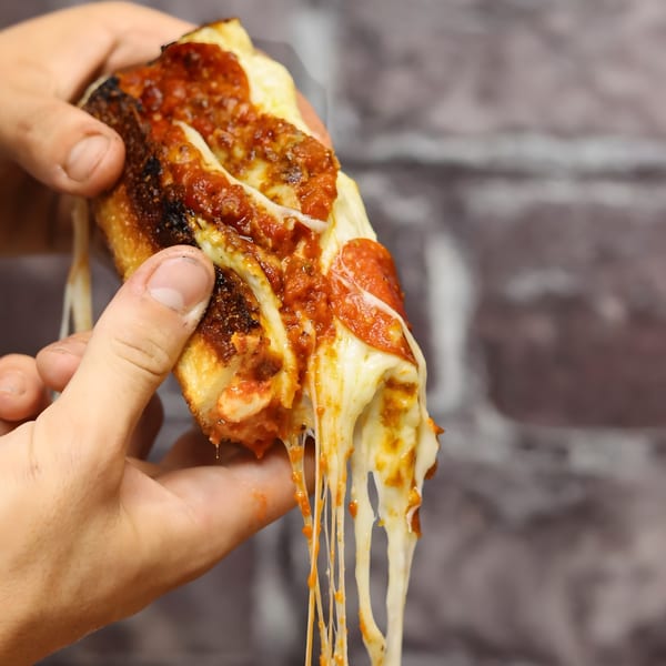 Hands holding a slice of Valentino's pepperoni pizza with abundant, stringy melted cheese and sauce.