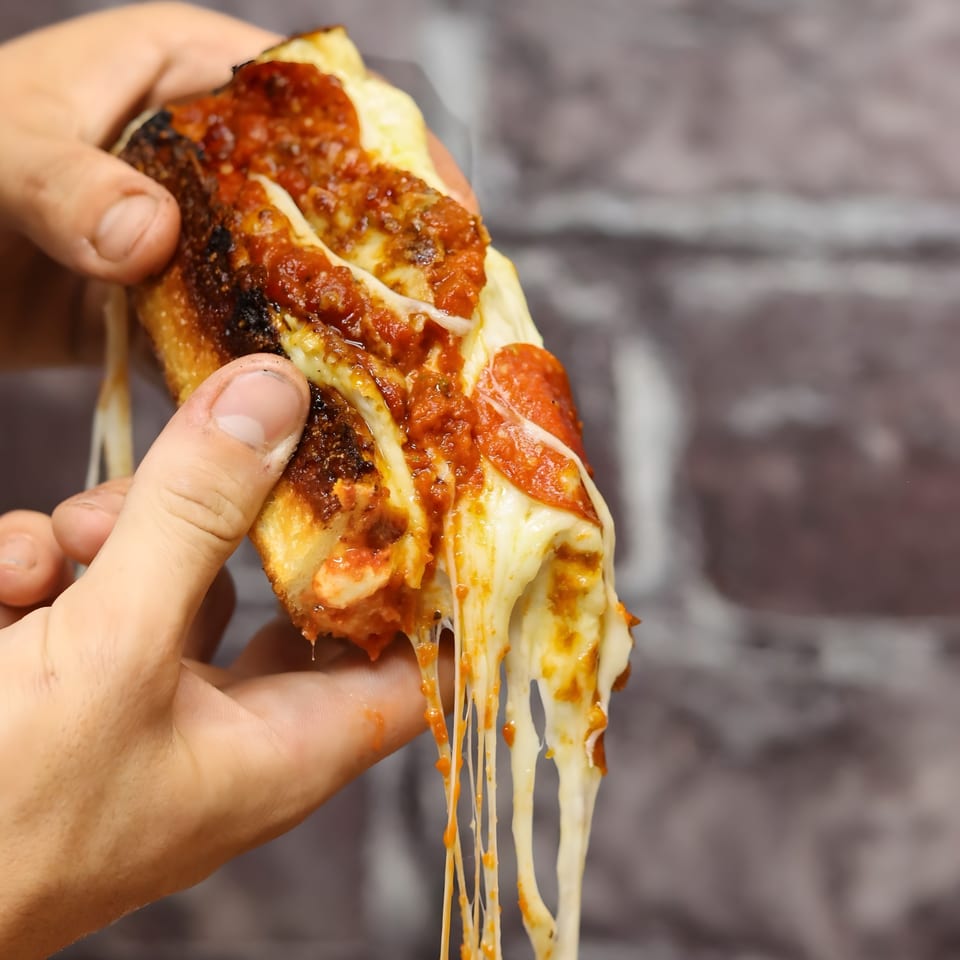 Hands holding a slice of Valentino's pepperoni pizza with abundant, stringy melted cheese and sauce.