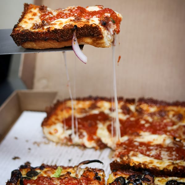A square slice of Valentino's Pizza PCH with melted cheese and sauce being lifted from a box.