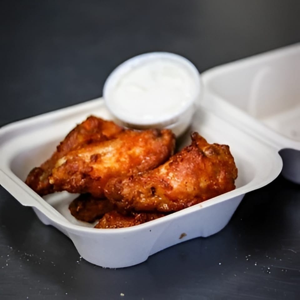 Valentino's Pizza PCH chicken wings with dipping sauce in a white takeout container.