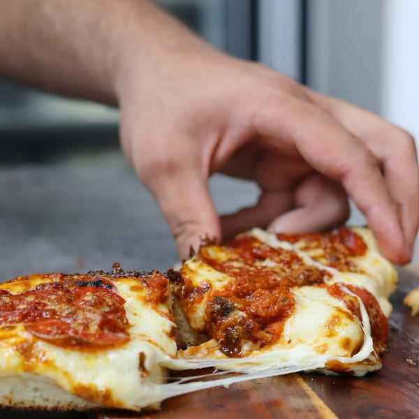 A hand pulls a slice of Valentino's pepperoni pizza, stretching the melted cheese.