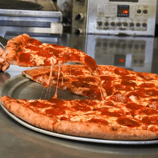A hand lifts a slice of pepperoni pizza from a large pie on a metal tray, with cheese stretching.