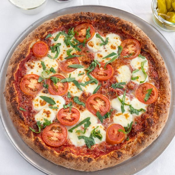 Valentino's Pizza PCH Margherita pizza with fresh tomatoes, mozzarella, and basil on a metal tray.